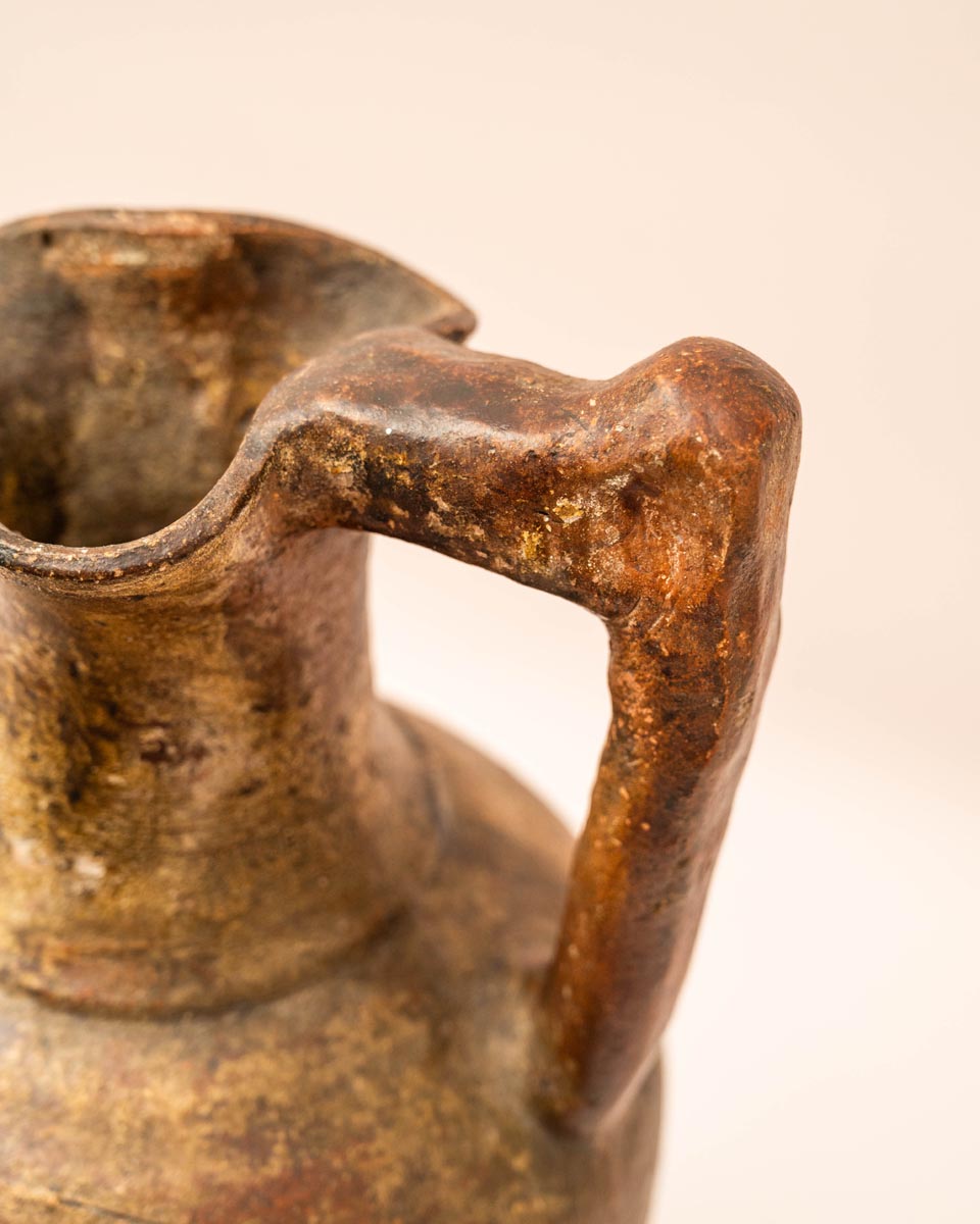 Handgemaakte aardewerken kruik met hoekig handvat en rustiek oppervlak