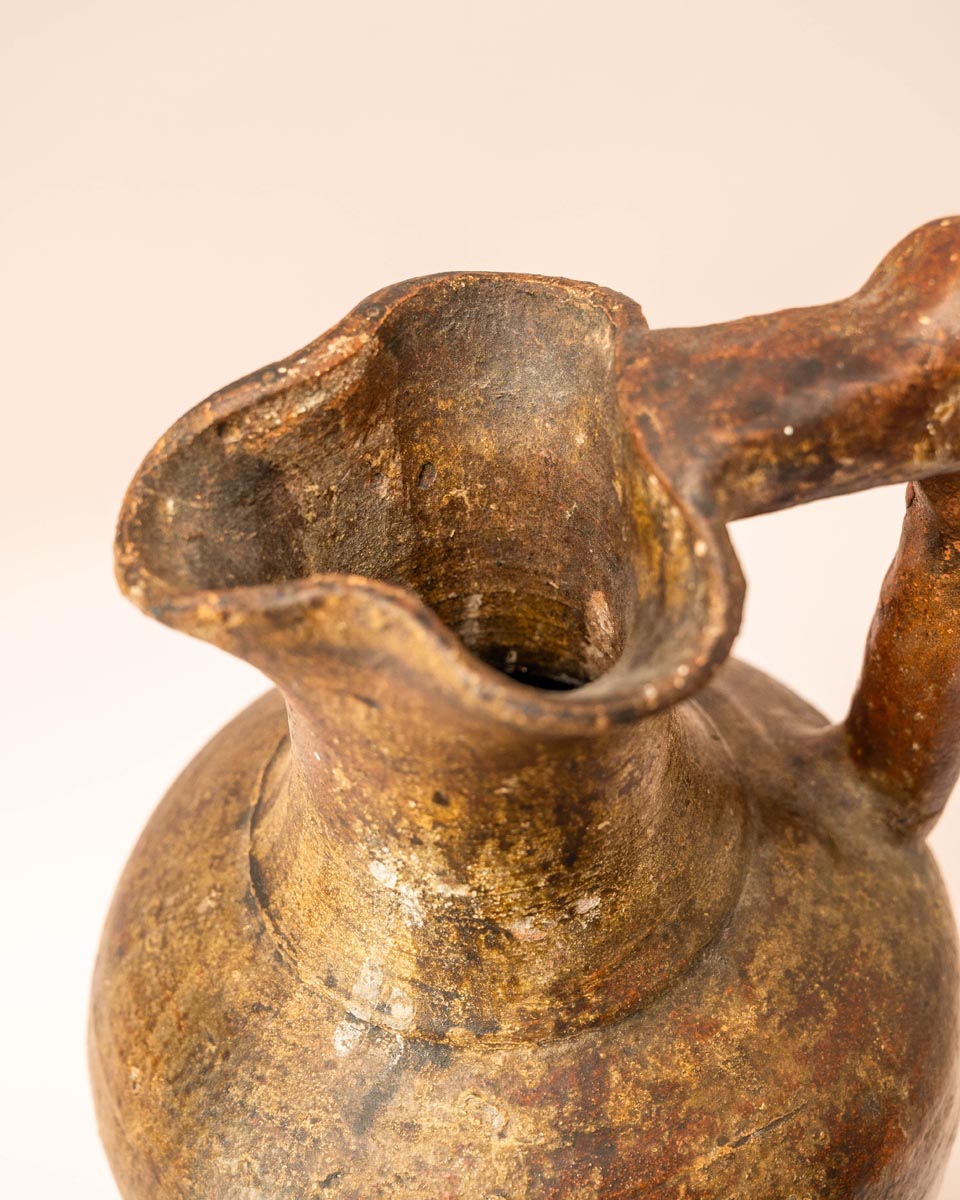 Handgemaakte aardewerken kruik met hoekig handvat en rustiek oppervlak