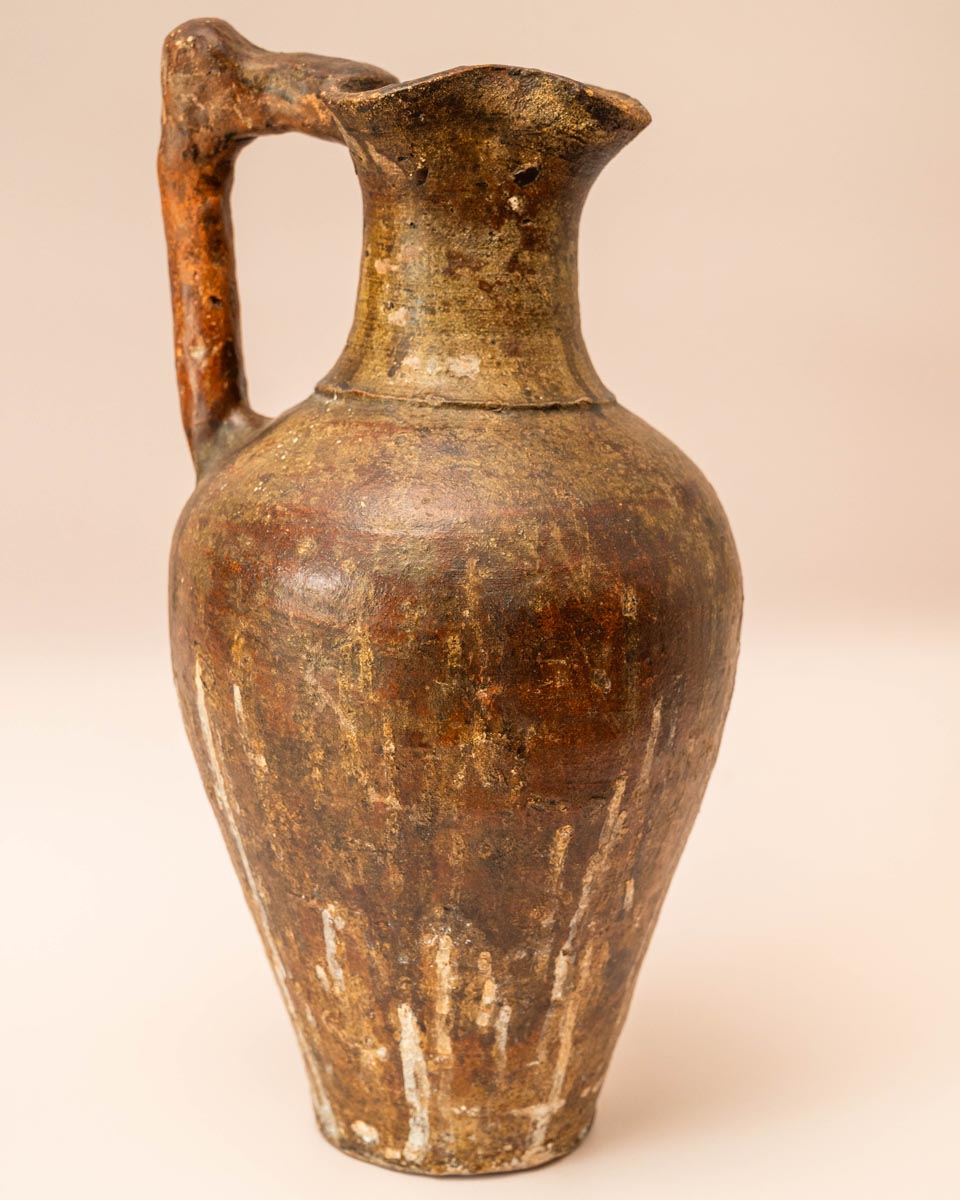 Handgemaakte aardewerken kruik met hoekig handvat en rustiek oppervlak